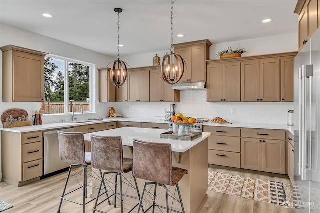 kitchen featuring a breakfast bar, a sink, high quality appliances, light wood-type flooring, and under cabinet range hood