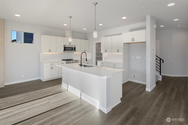 kitchen with dark wood-style flooring, tasteful backsplash, stainless steel microwave, a sink, and an island with sink