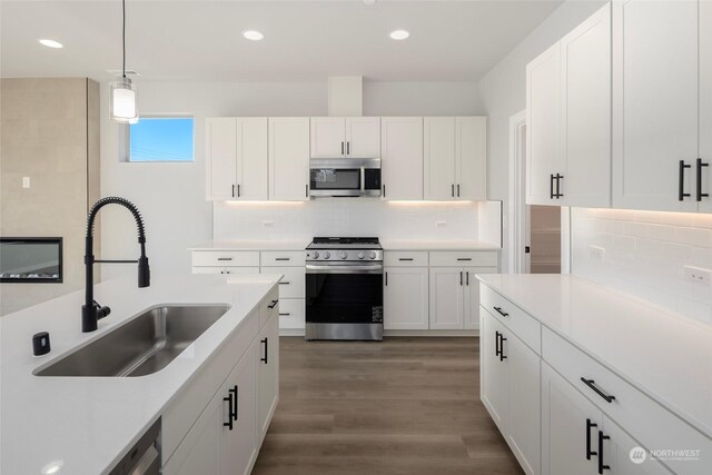 kitchen with appliances with stainless steel finishes, hanging light fixtures, light countertops, white cabinetry, and a sink