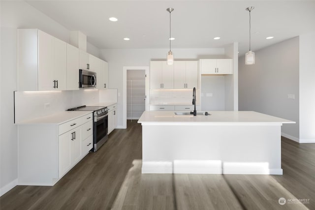 kitchen featuring a center island with sink, dark wood-style floors, appliances with stainless steel finishes, light countertops, and a sink