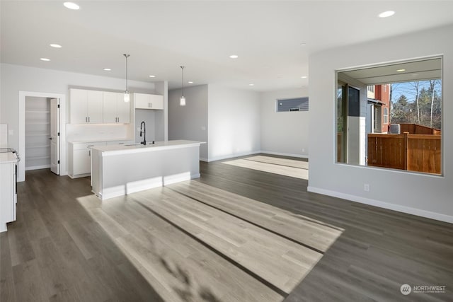 unfurnished living room featuring recessed lighting, baseboards, dark wood-type flooring, and a sink