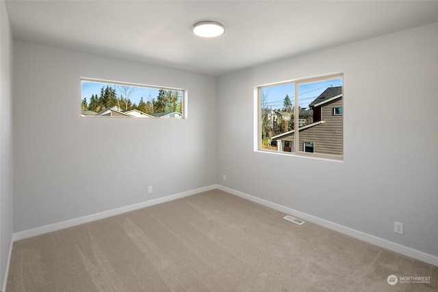 empty room featuring baseboards, plenty of natural light, visible vents, and light colored carpet