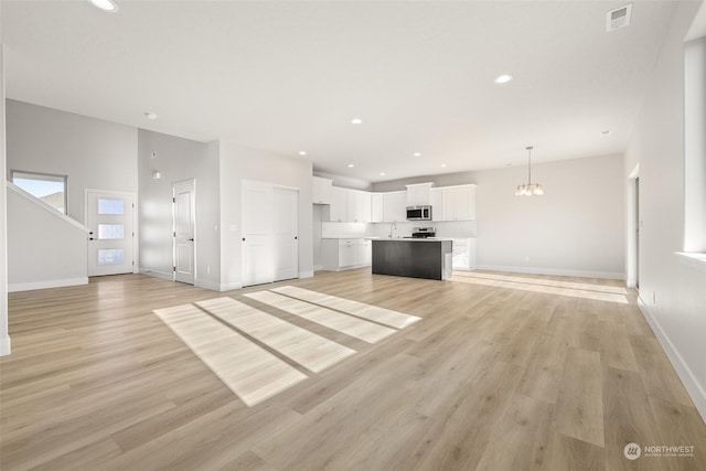 unfurnished living room featuring an inviting chandelier and light hardwood / wood-style flooring