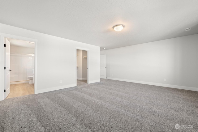 unfurnished bedroom with connected bathroom, a walk in closet, a textured ceiling, a closet, and light colored carpet