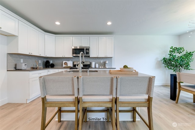 kitchen featuring a kitchen island with sink, white cabinetry, light hardwood / wood-style flooring, and a kitchen breakfast bar