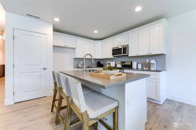 kitchen featuring an island with sink, sink, appliances with stainless steel finishes, white cabinets, and light hardwood / wood-style floors