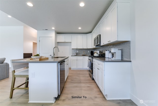 kitchen with light hardwood / wood-style flooring, appliances with stainless steel finishes, an island with sink, sink, and white cabinetry