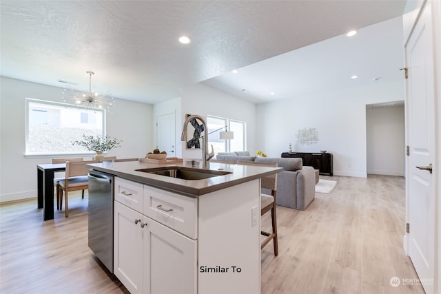 kitchen featuring light wood-type flooring, decorative light fixtures, white cabinetry, sink, and a center island with sink