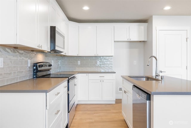 kitchen featuring sink, white cabinetry, light hardwood / wood-style flooring, appliances with stainless steel finishes, and an island with sink