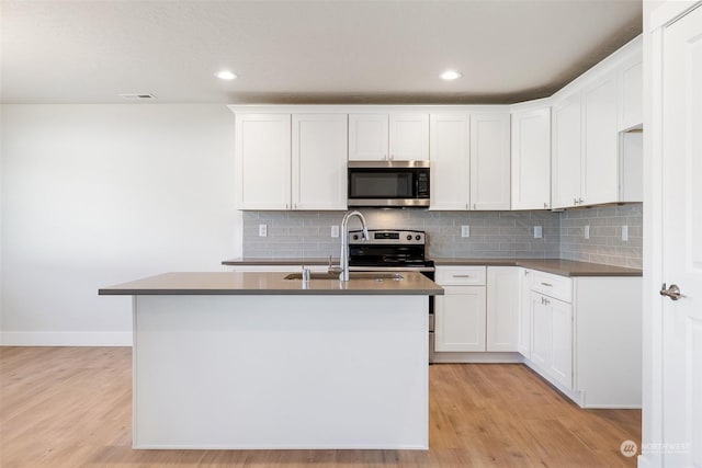 kitchen featuring sink, light hardwood / wood-style flooring, white cabinets, a center island with sink, and decorative backsplash