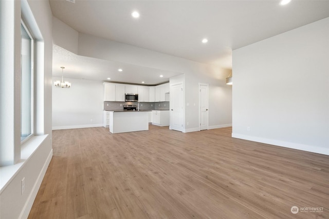 unfurnished living room featuring an inviting chandelier and light hardwood / wood-style flooring