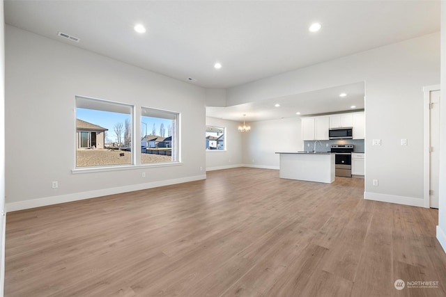 unfurnished living room featuring sink, a notable chandelier, and light wood-type flooring