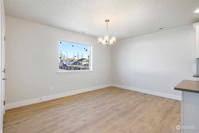 unfurnished dining area with a textured ceiling, an inviting chandelier, and light hardwood / wood-style flooring