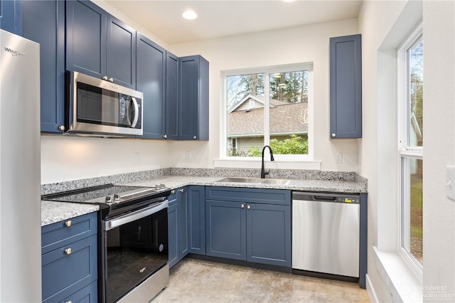 kitchen with blue cabinets, stainless steel appliances, sink, and light stone countertops