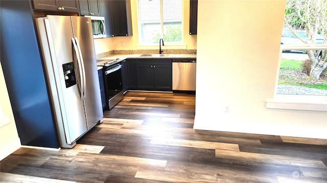 kitchen with appliances with stainless steel finishes, light stone counters, dark hardwood / wood-style floors, and sink