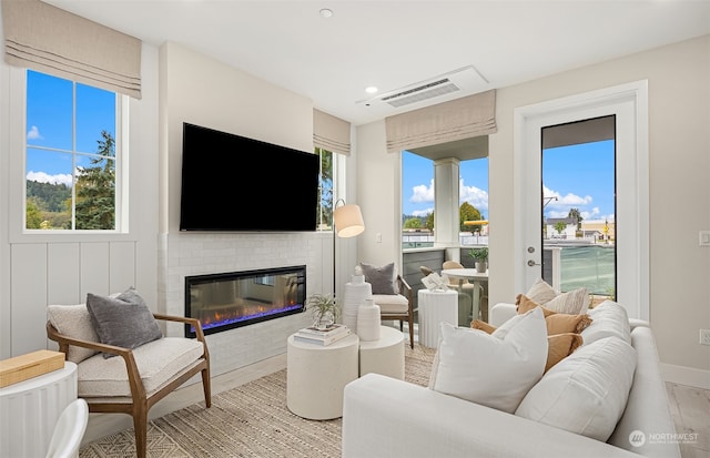 living room featuring a brick fireplace, light hardwood / wood-style flooring, and a wealth of natural light