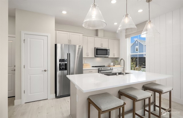 kitchen featuring an island with sink, stainless steel appliances, white cabinetry, and hanging light fixtures