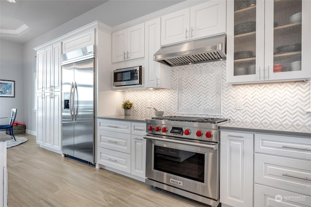 kitchen featuring decorative backsplash, light wood-style floors, white cabinetry, built in appliances, and under cabinet range hood