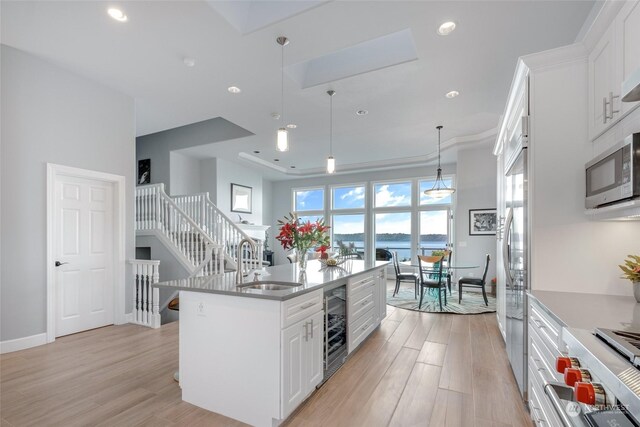 kitchen featuring white cabinets, hanging light fixtures, stainless steel appliances, light hardwood / wood-style floors, and a kitchen island with sink