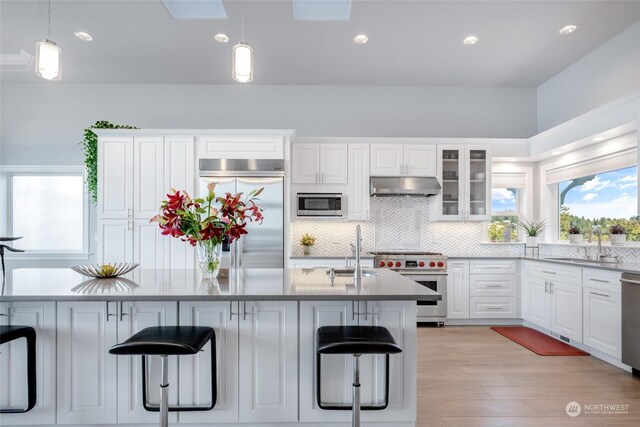 kitchen with built in appliances, light hardwood / wood-style flooring, a kitchen breakfast bar, range hood, and hanging light fixtures