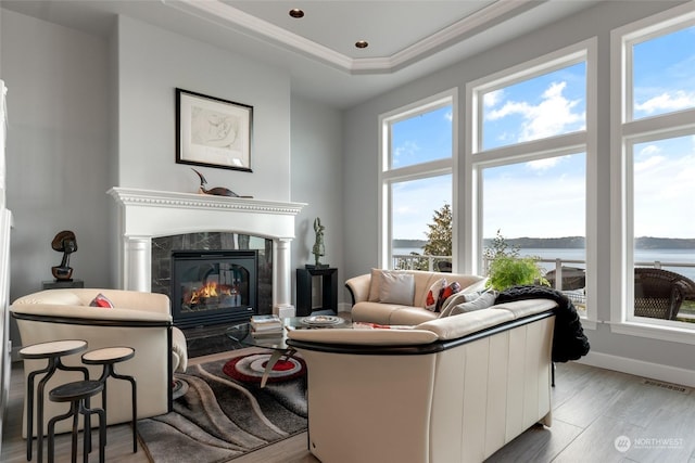 living area with light wood-style flooring, a premium fireplace, a water view, visible vents, and baseboards