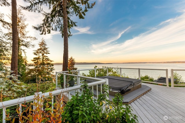 deck at dusk with a water view and a covered hot tub