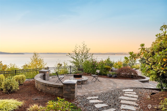 patio terrace at dusk featuring an outdoor fire pit and a water view