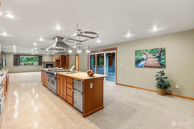 kitchen featuring sink, a center island with sink, wall chimney exhaust hood, range with two ovens, and butcher block counters