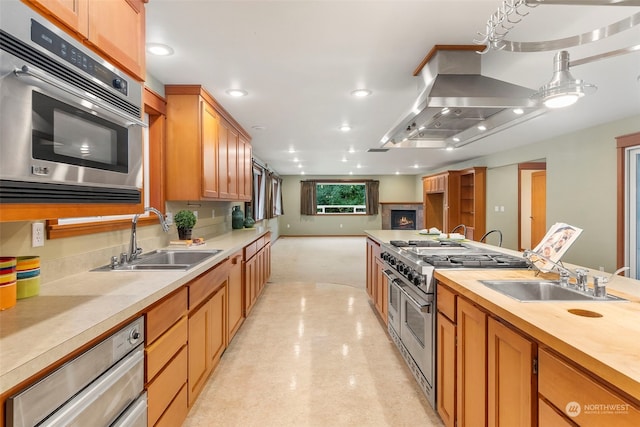 kitchen featuring island range hood, decorative light fixtures, appliances with stainless steel finishes, and sink