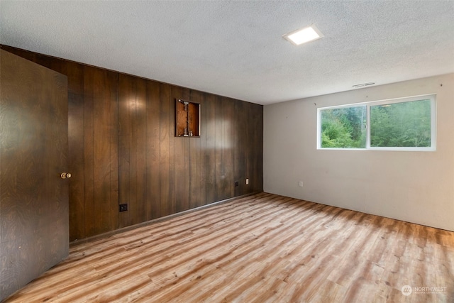 unfurnished room featuring wood walls, light hardwood / wood-style floors, and a textured ceiling