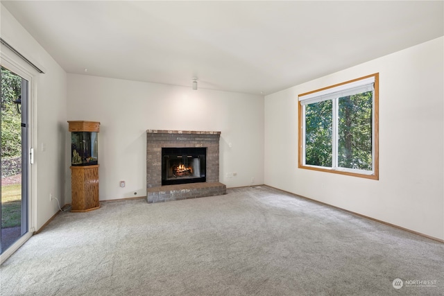 unfurnished living room with a wealth of natural light, light colored carpet, and a brick fireplace