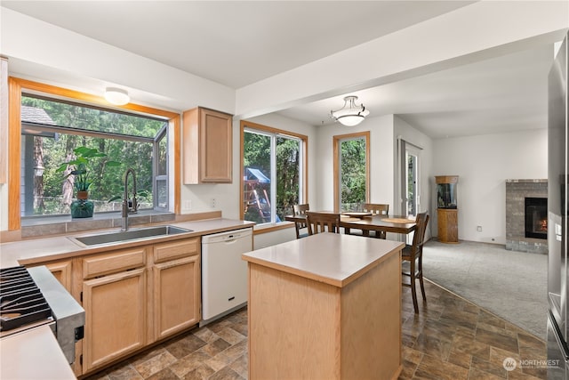 kitchen with a fireplace, white dishwasher, sink, dark colored carpet, and light brown cabinets