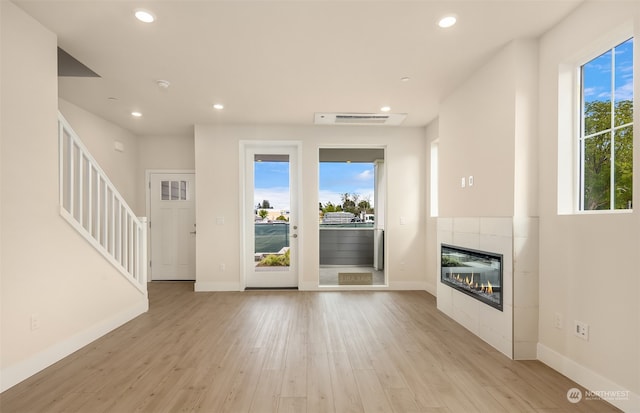 unfurnished living room with a tiled fireplace and light hardwood / wood-style flooring