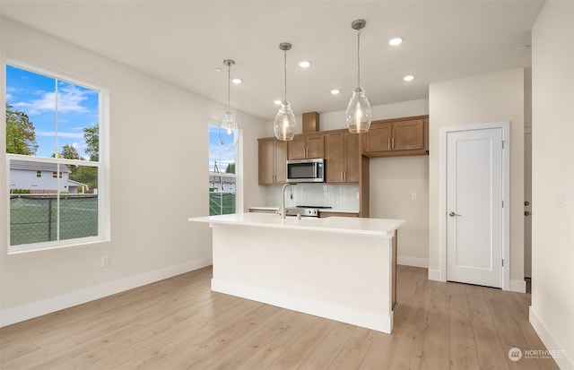 kitchen featuring light hardwood / wood-style floors, sink, an island with sink, hanging light fixtures, and backsplash