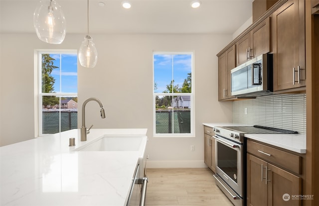 kitchen with light stone counters, pendant lighting, sink, appliances with stainless steel finishes, and light hardwood / wood-style floors