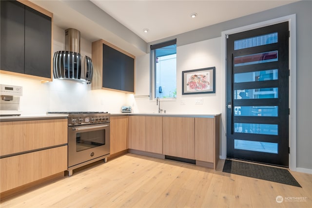 kitchen featuring high end stainless steel range, ventilation hood, light brown cabinetry, and light wood-type flooring