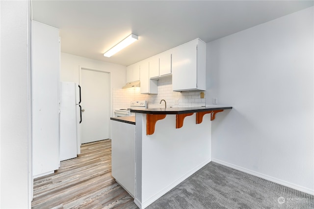 kitchen with light hardwood / wood-style flooring, white appliances, white cabinetry, tasteful backsplash, and a breakfast bar