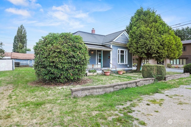 view of front of house with a chimney, covered porch, a front lawn, and a shingled roof