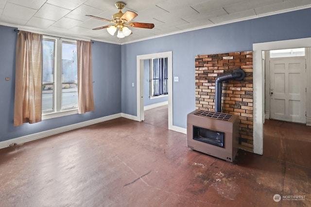 unfurnished living room featuring baseboards, ceiling fan, a wood stove, and crown molding