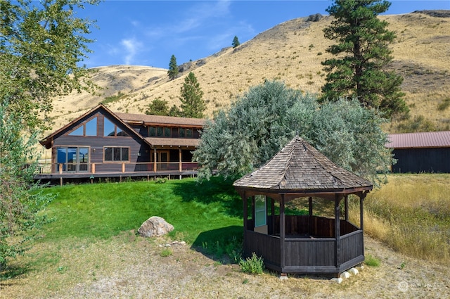 back of property with a deck with mountain view, a lawn, and a gazebo