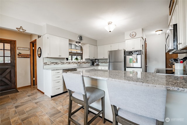 kitchen featuring white cabinets, light stone counters, stainless steel appliances, and kitchen peninsula