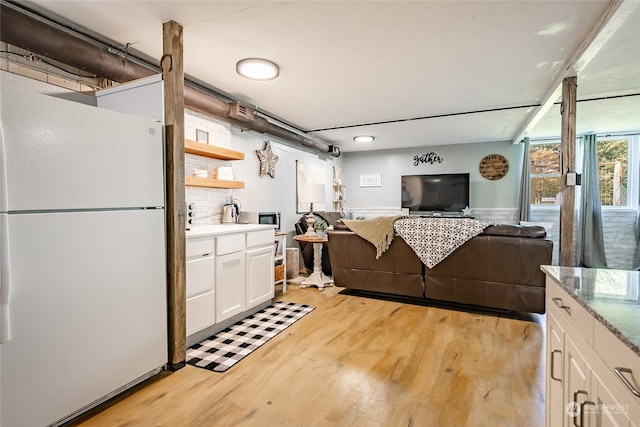 kitchen with white refrigerator, light stone countertops, light hardwood / wood-style floors, and white cabinets