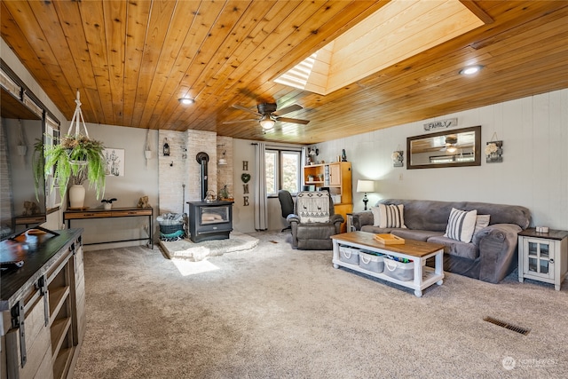 carpeted living room with wooden ceiling, a skylight, ceiling fan, and a wood stove