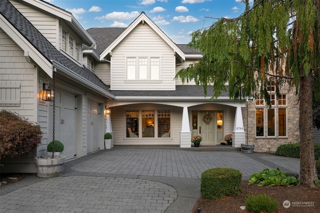 property entrance featuring a garage, decorative driveway, roof with shingles, and a porch