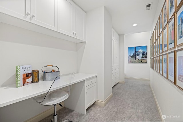 office space featuring baseboards, built in desk, visible vents, and light colored carpet