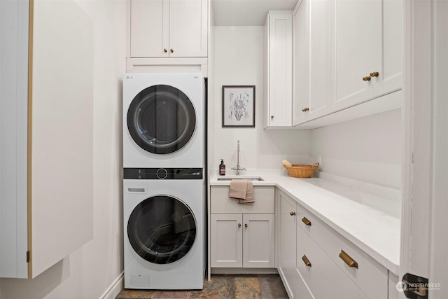 laundry room featuring stone finish flooring, cabinet space, a sink, and stacked washer and clothes dryer