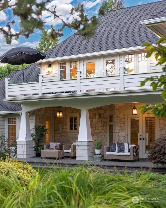 back of property with stone siding, a shingled roof, outdoor lounge area, and a balcony