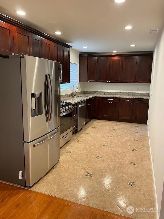 kitchen with light hardwood / wood-style flooring, appliances with stainless steel finishes, light stone counters, and sink