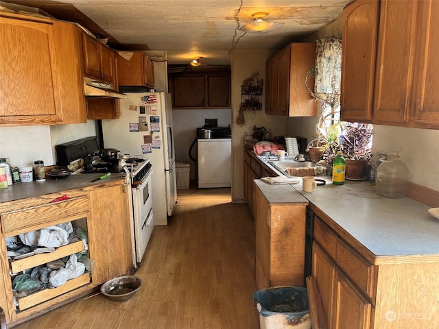 kitchen with a sink, light wood-style floors, white range with gas cooktop, brown cabinets, and washer / dryer