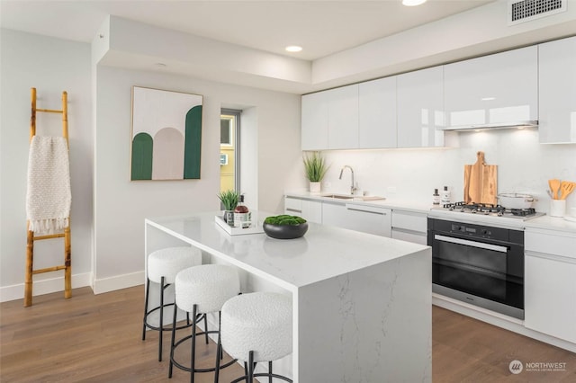 kitchen with visible vents, oven, dark wood finished floors, stainless steel gas stovetop, and a sink